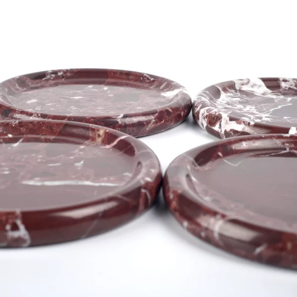 Four round burgundy marble trays with stunning natural red patches and white veining, placed side by side, polished to a smooth and reflective finish.