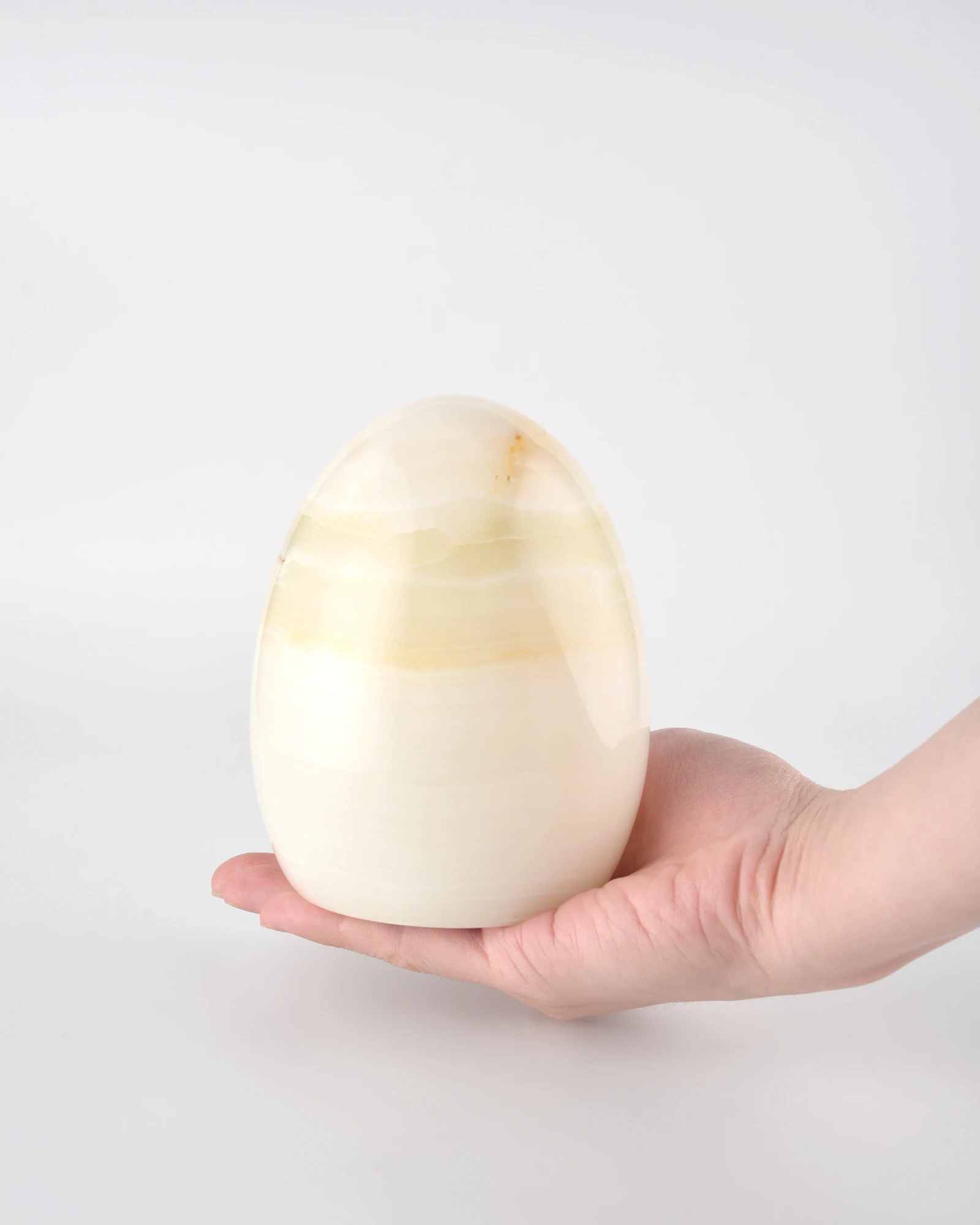 Compact and delicate Egg-Shaped Onyx Tap Lamp held in the palm, showcasing its translucent onyx material and smooth mirror-like finish