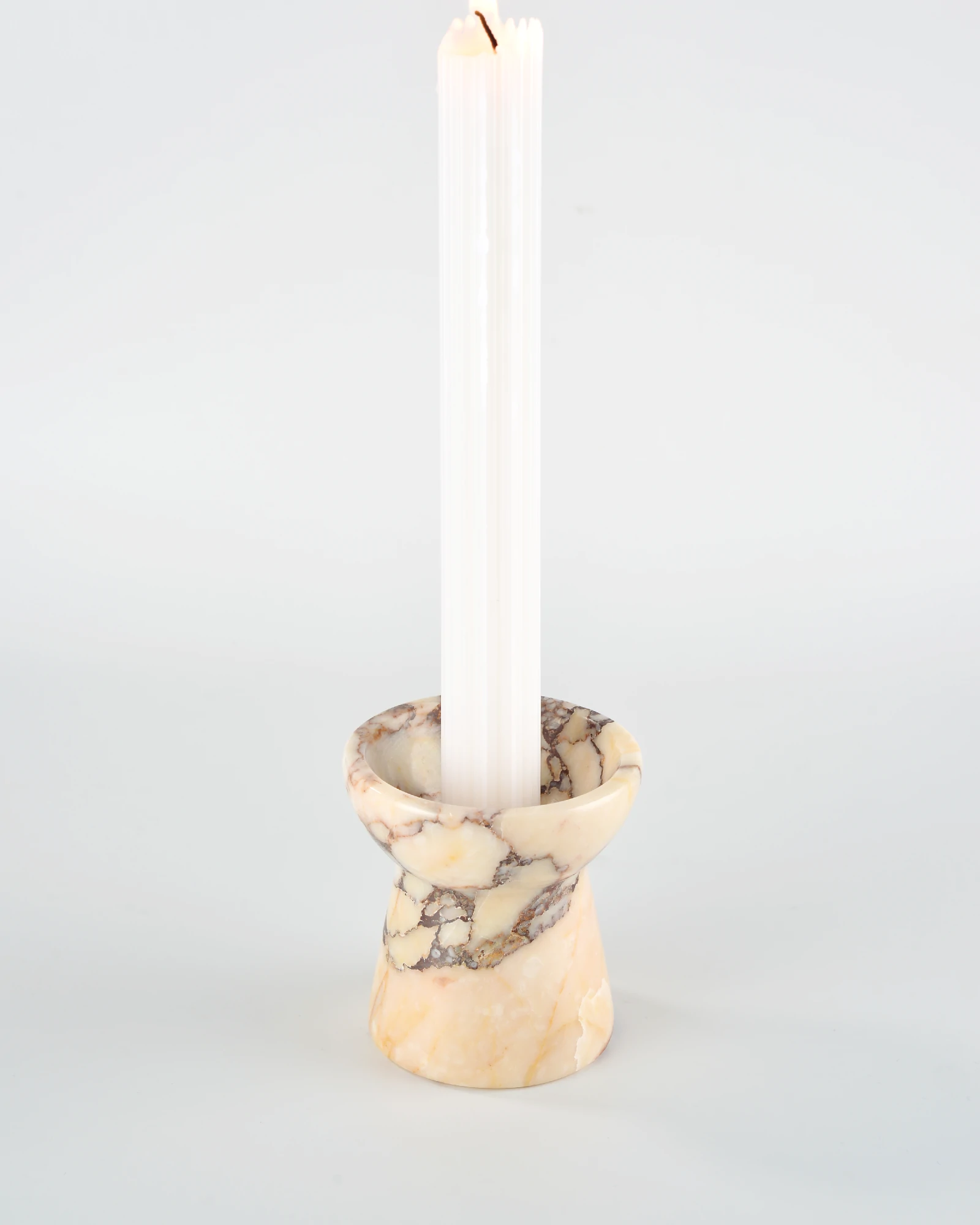 Long rectangular aromatherapy candle placed on Calacatta Marble candle holder shaped like a small torch, emphasizing its luxurious design