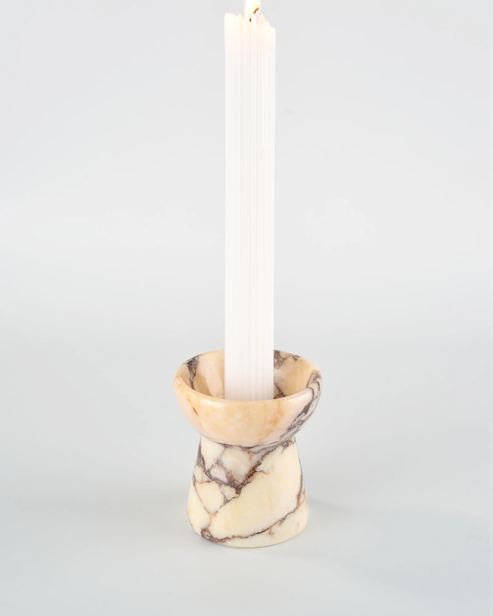 Long aromatherapy candle resting on the Calacatta Marble candle holder shaped like a small torch, showcasing its elegant design