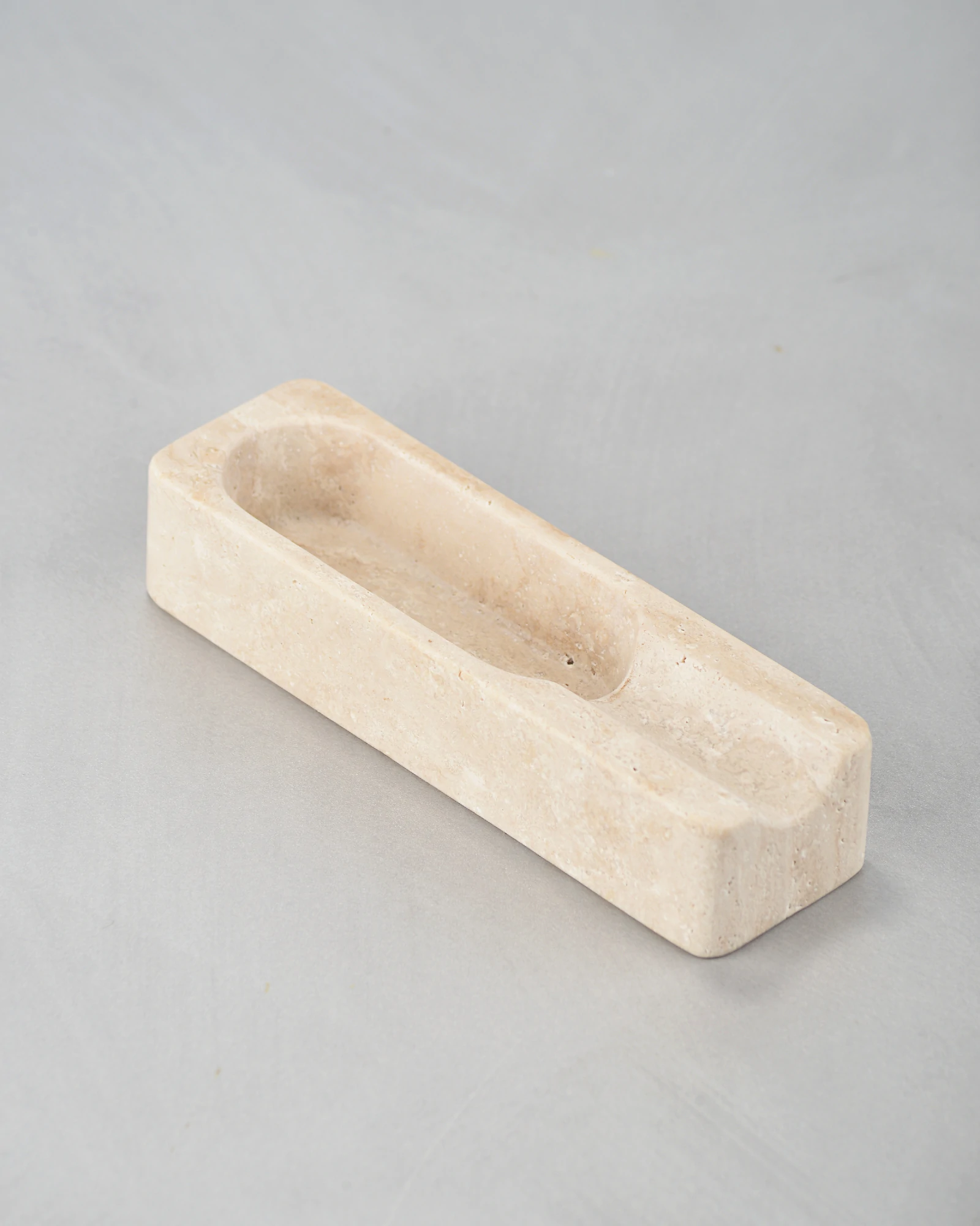 Angled view of travertine cigar ashtray showing carved details and natural pores