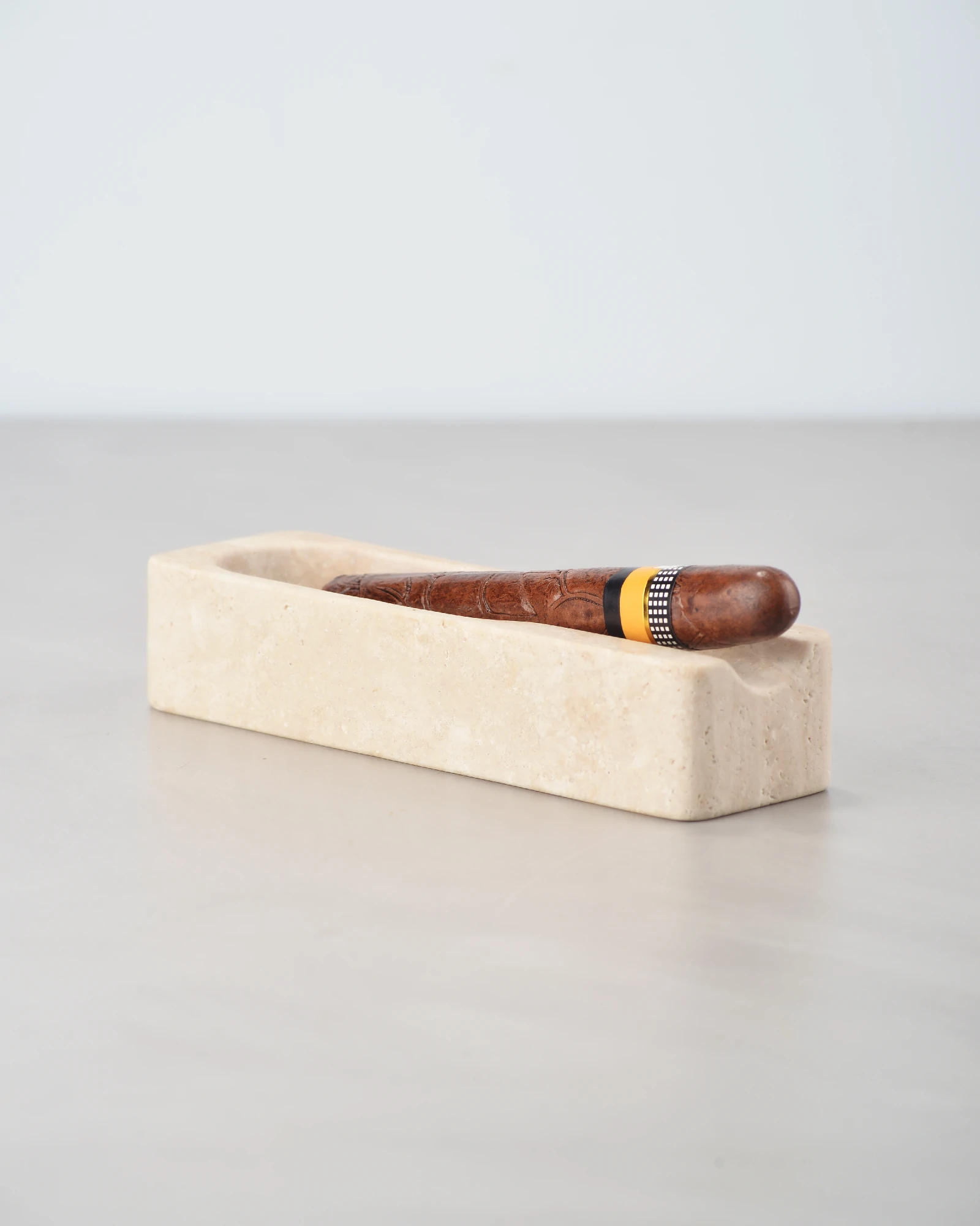 Travertine cigar ashtray with cigar placed on glossy table, creating a reflection