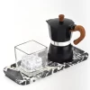 Coffee pot and glass cup arranged on black marble tray