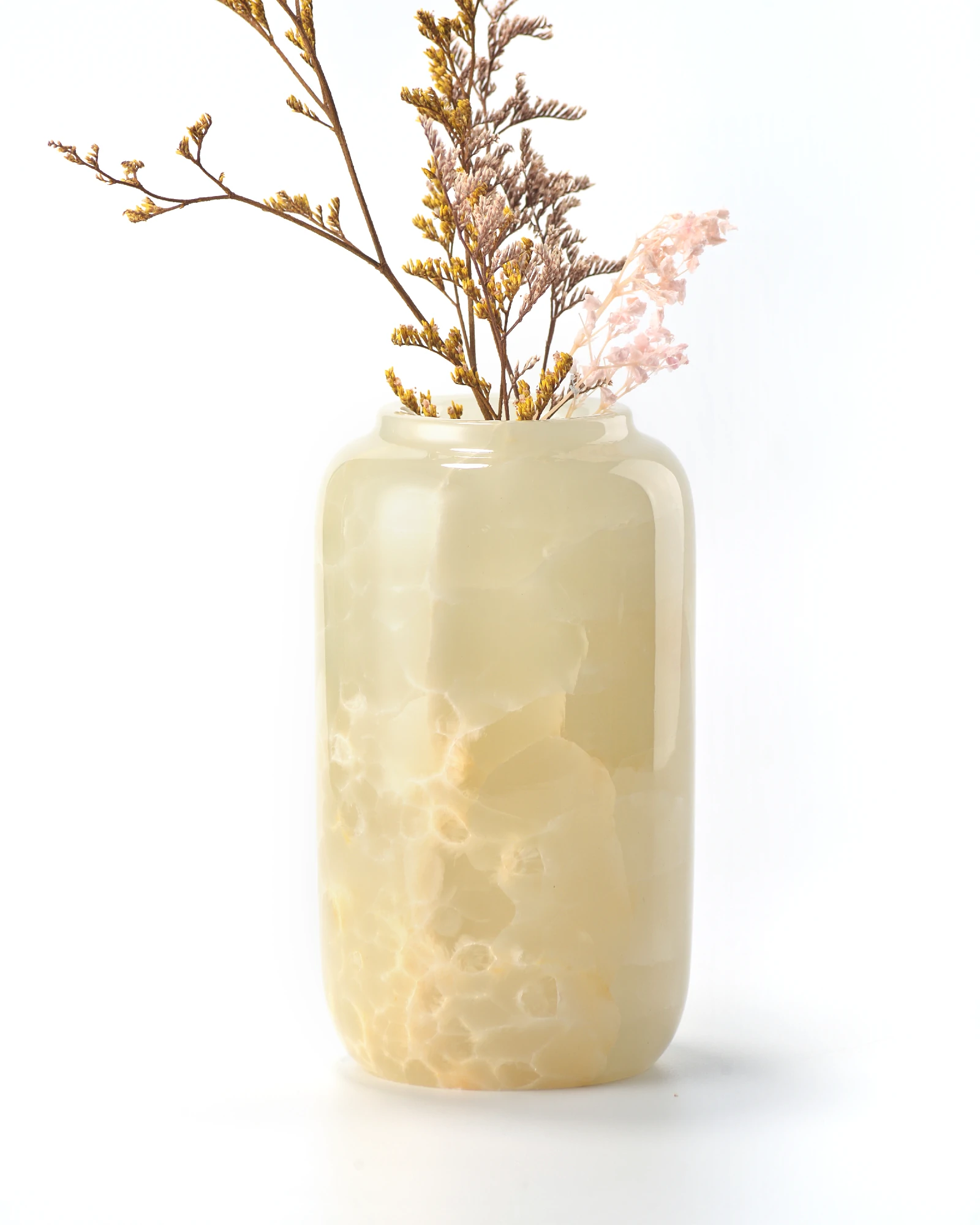 Green onyx vase with light-colored dried flowers reflecting on stone surface